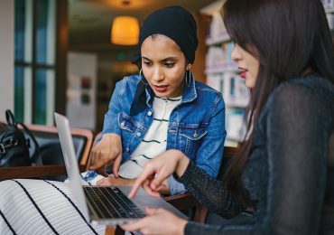 Two women working together on a laptop in the library
